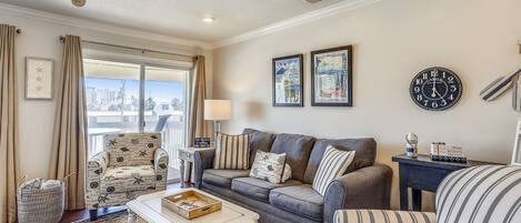A living room with a sofa, armchairs, a coffee table, a side table, a clock, and a window with curtains.