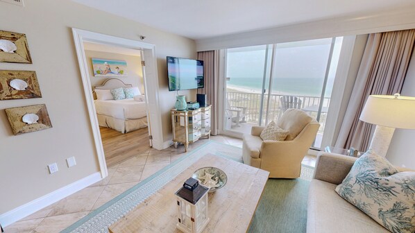A hotel room with a bed, a TV, a view of the beach, and a balcony.