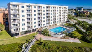 Ein mehrstöckiges Hotel mit Balkonen, einem Schwimmbad und umliegender Bepflanzung.