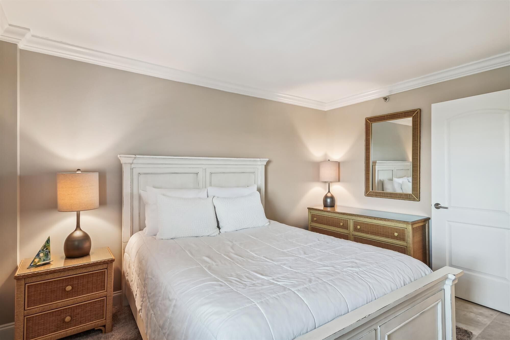 Une chambre à coucher bien rangée, avec un lit, deux tables de chevet, une commode, une coiffeuse, un miroir et une porte.
