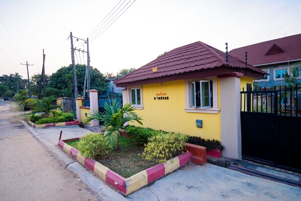 A yellow house with a red roof, a black gate, and a small garden with plants.