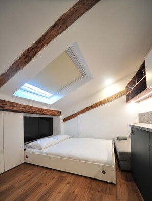 Une chambre dotée d’une lucarne, de poutres apparentes, d’un lit, d’une petite table de chevet et d’une armoire intégrée.