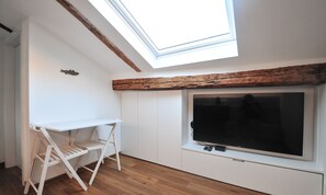 Une pièce dotée d’une lucarne, d’un téléviseur et d’un bureau blanc avec une chaise.