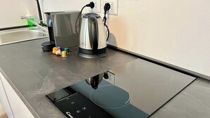 Une cuisine moderne équipée d’une plaque de cuisson à induction intégrée, d’une bouilloire et d’une machine à café posées sur le plan de travail.