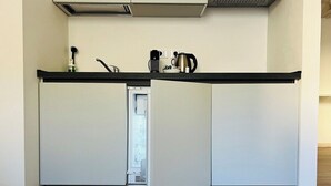 Une cuisine de taille réduite avec un plan de travail noir, des placards blancs et un réfrigérateur bien visible.