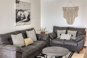 A modern living room with a grey sofa, a round coffee table, and a macrame wall hanging. - 6th-floor apt near beach with pool views, outdoor pool, balcony, streaming, W/D (Jaco)