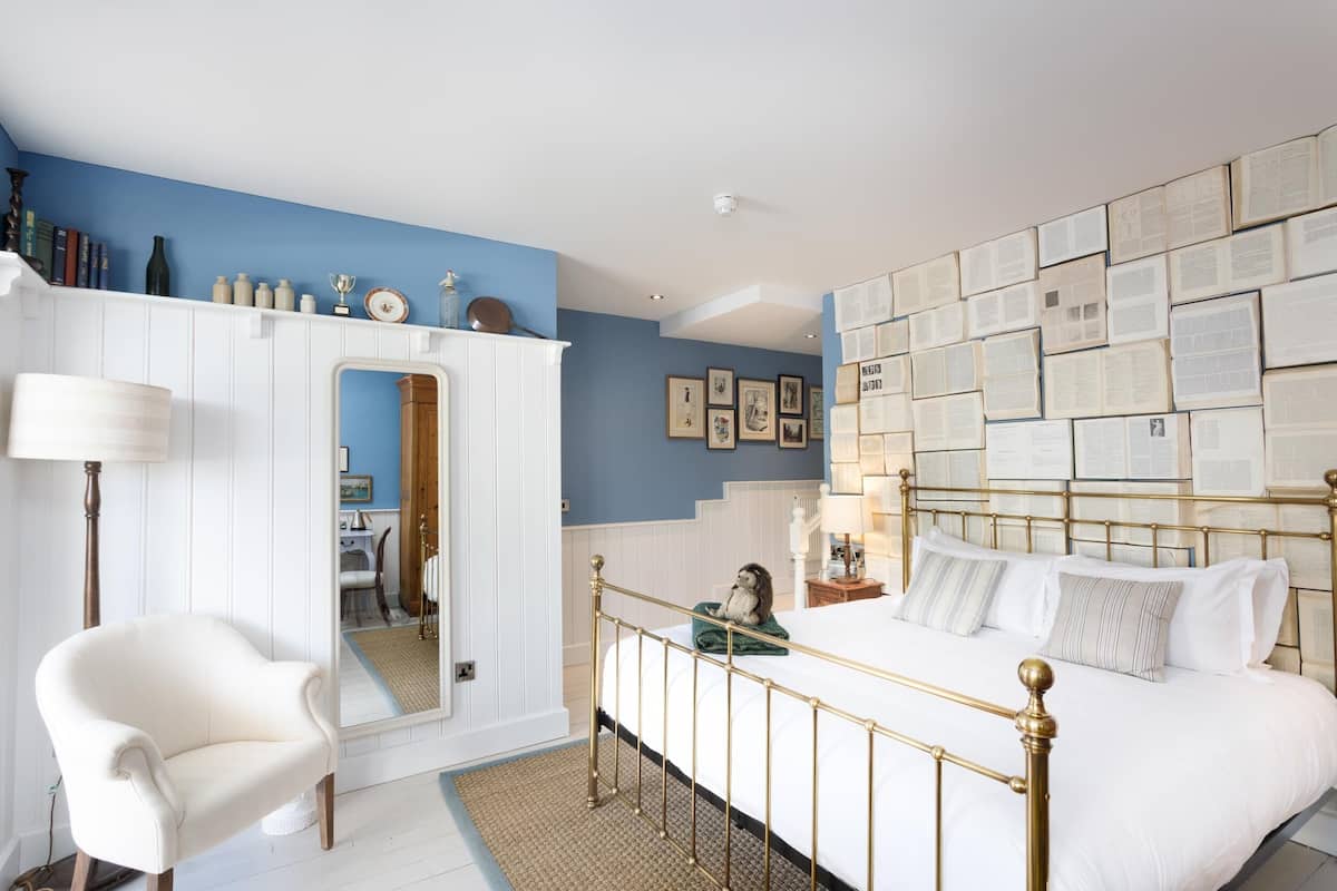 A bedroom with a bed, a chair, a wardrobe, and a wall covered with books.