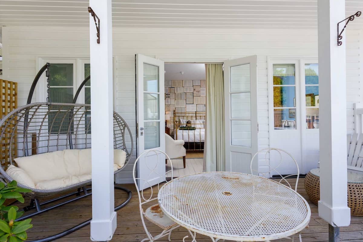 A covered outdoor area with a white metal table and chairs, a wicker swing chair, and a wooden deck.