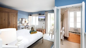 A bedroom with a bed, bedside table, and a television. There is a bathroom with a bathtub and a sink. - The Boathouse (Bath)