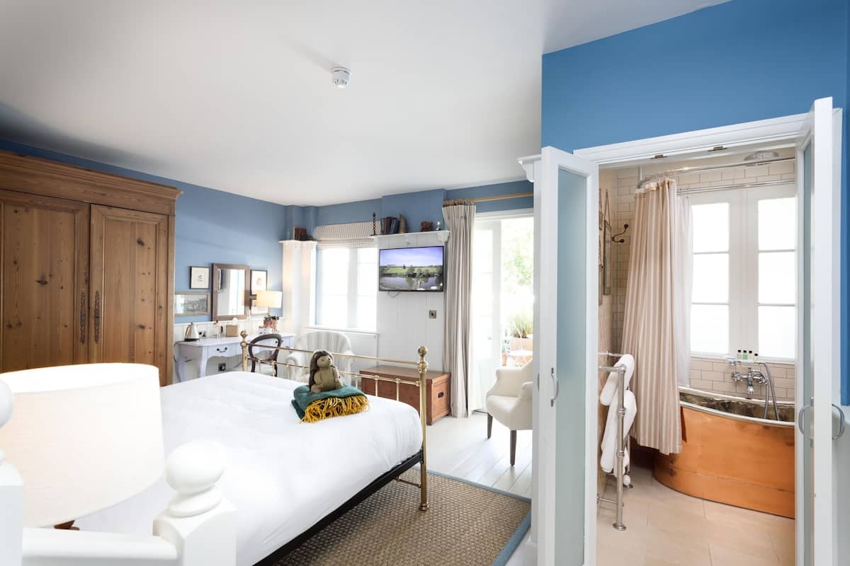 A bedroom with a bed, bedside table, and a television. There is a bathroom with a bathtub and a sink.