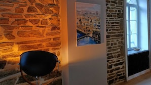 Een kamer met stenen muren, een schilderij van een stadsgezicht, een zwarte lamp en een raam met uitzicht.