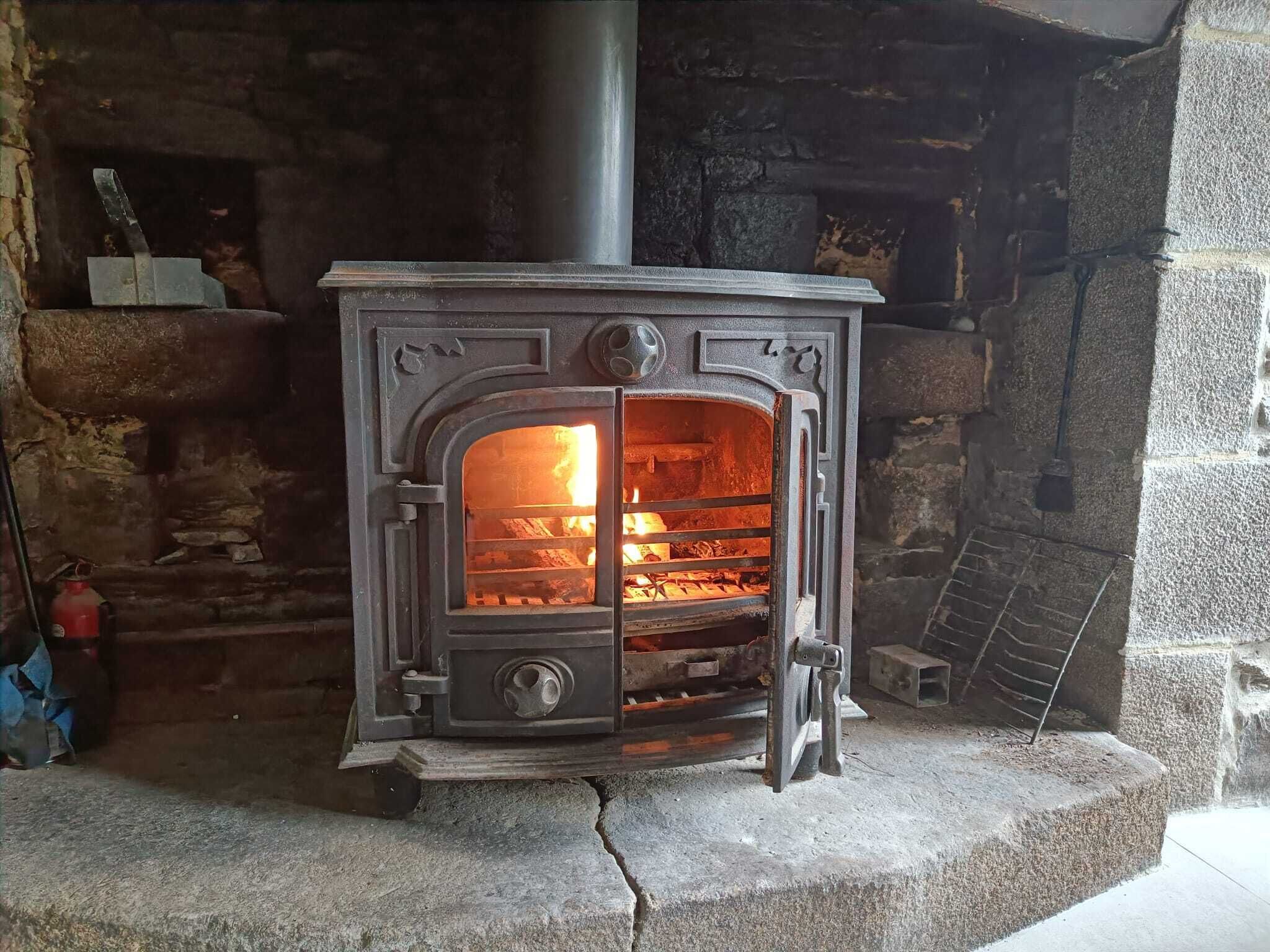 Una chimenea de piedra con una puerta metálica, una chimenea y fuego ardiendo en su interior.