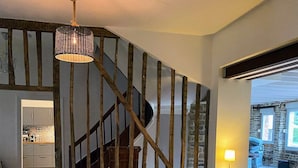 Een ruime eethoek met een grote houten tafel, zwarte stoelen, een hanglamp en een stenen trap.