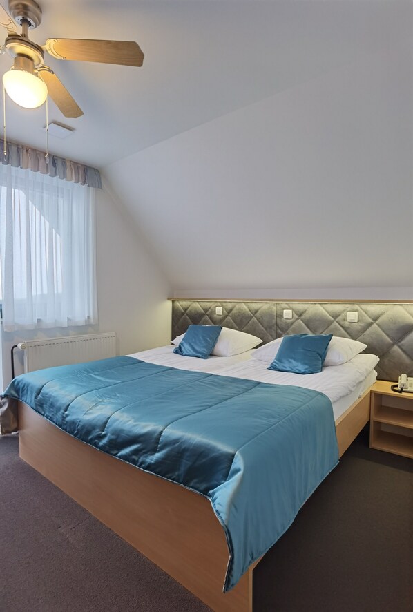 A hotel room with a bed, a ceiling fan, a bedside table, and a window with curtains. - Suite 15&17 (Gornji Grad)