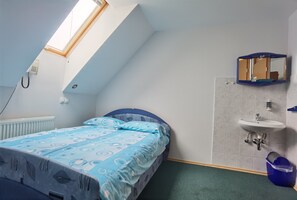 A bedroom with a sloped ceiling, a bed with a blue patterned bedspread, a small bathroom with a sink and mirror, and a skylight. - Suite 15&17 (Gornji Grad)