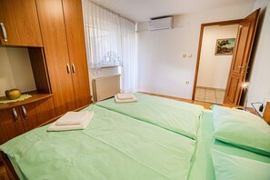 A room with two beds, wooden wardrobe, white curtains, radiator, and a painting on the wall. - Split three bedroom apartment with terrace (Podcetrtek)