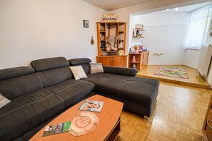 A living room with a dark grey sectional sofa, a wooden coffee table with magazines, and a wooden cabinet with various items. - Split three bedroom apartment with terrace (Podcetrtek)