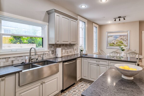 A modern kitchen with white cabinetry, a stainless steel sink, and a marble countertop.