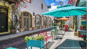 Una calle con un café llamado "Peace Pie" que ofrece sándwiches, mesas al aire libre con sombrillas, y un edificio con ventanas de arco y fachada blanca.