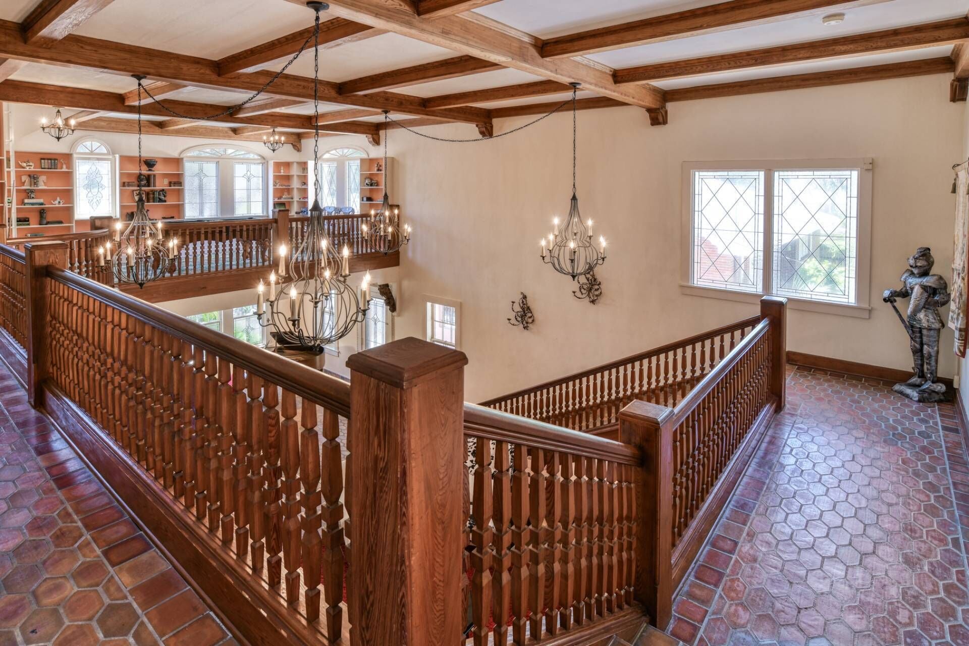 Um interior espaçoso com escada de madeira, vários candelabros e uma estátua.