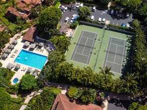 Vue aérienne d’un complexe hôtelier doté d’une piscine, de courts de tennis et d’une végétation luxuriante.
