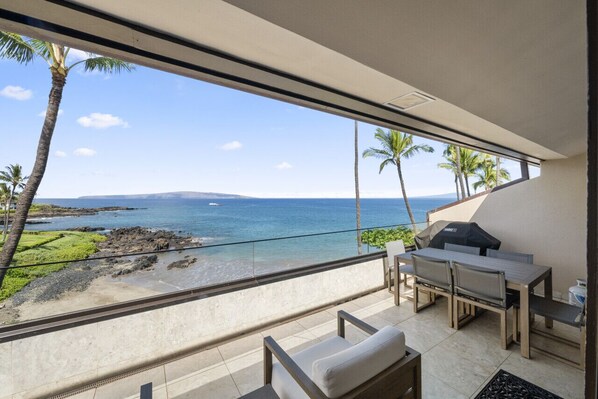A balcony with a view of the ocean, a table with chairs, and a grill.