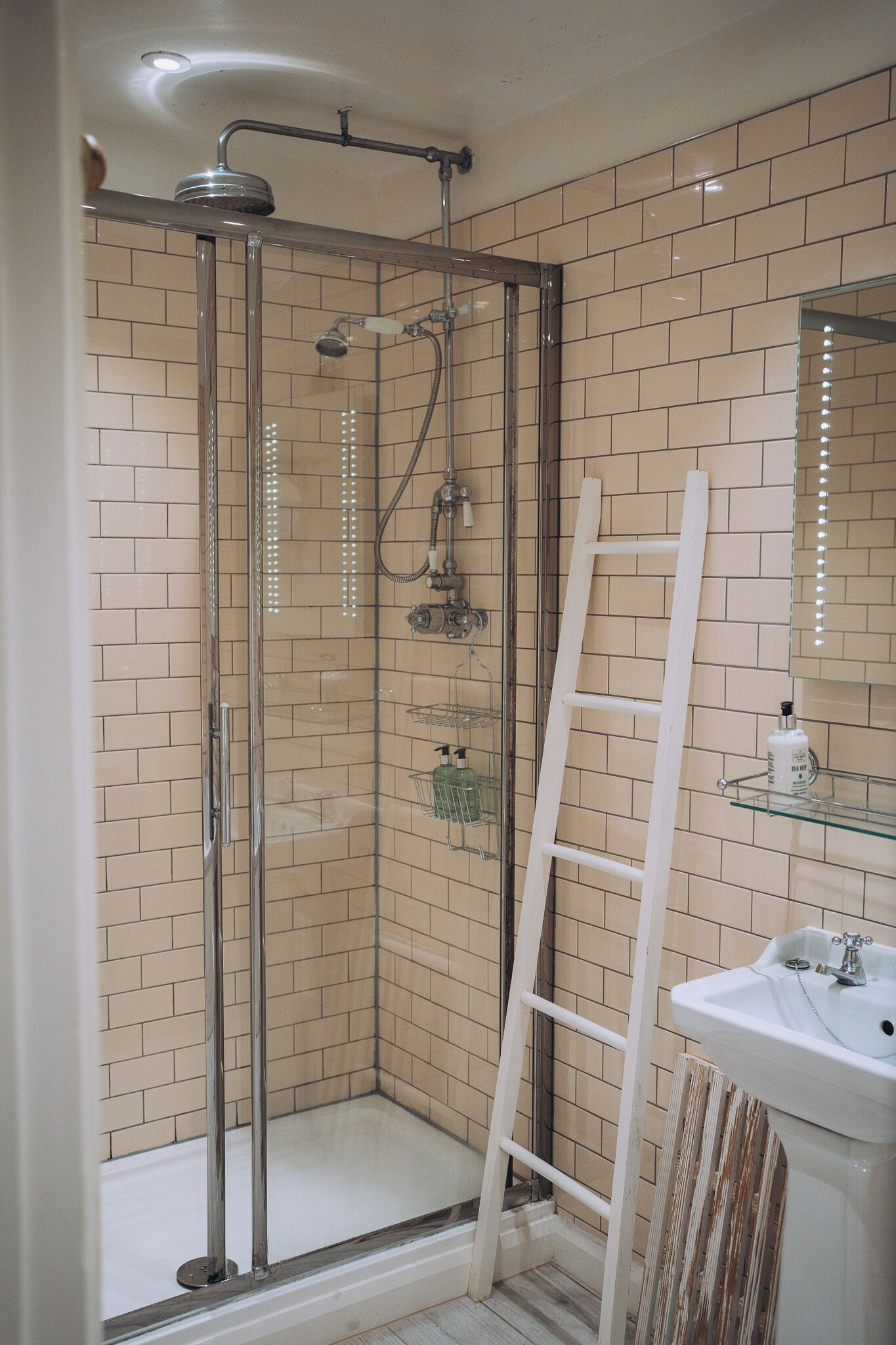 A glass-enclosed shower with a metal frame, a white sink, and a mirror above it.