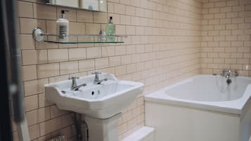 A bathroom with a white sink, a bathtub, and a glass shelf with toiletries.