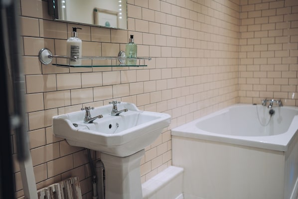 Een badkamer met een wit wastafelmeubel, een badkuip en een glazen plank met toiletartikelen.