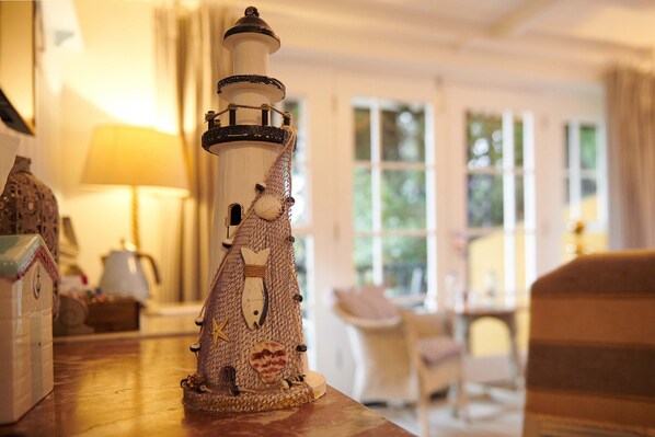 A lighthouse model on a table in a warmly lit room with a view of greenery outside. - The Ness House (Teignmouth)