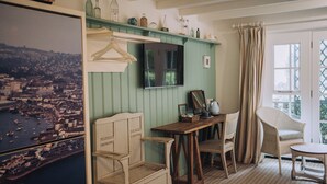 A room with a wooden desk, a chair, a hanging coat rack, a television, and a large framed picture of a cityscape. - The Ness House (Teignmouth)