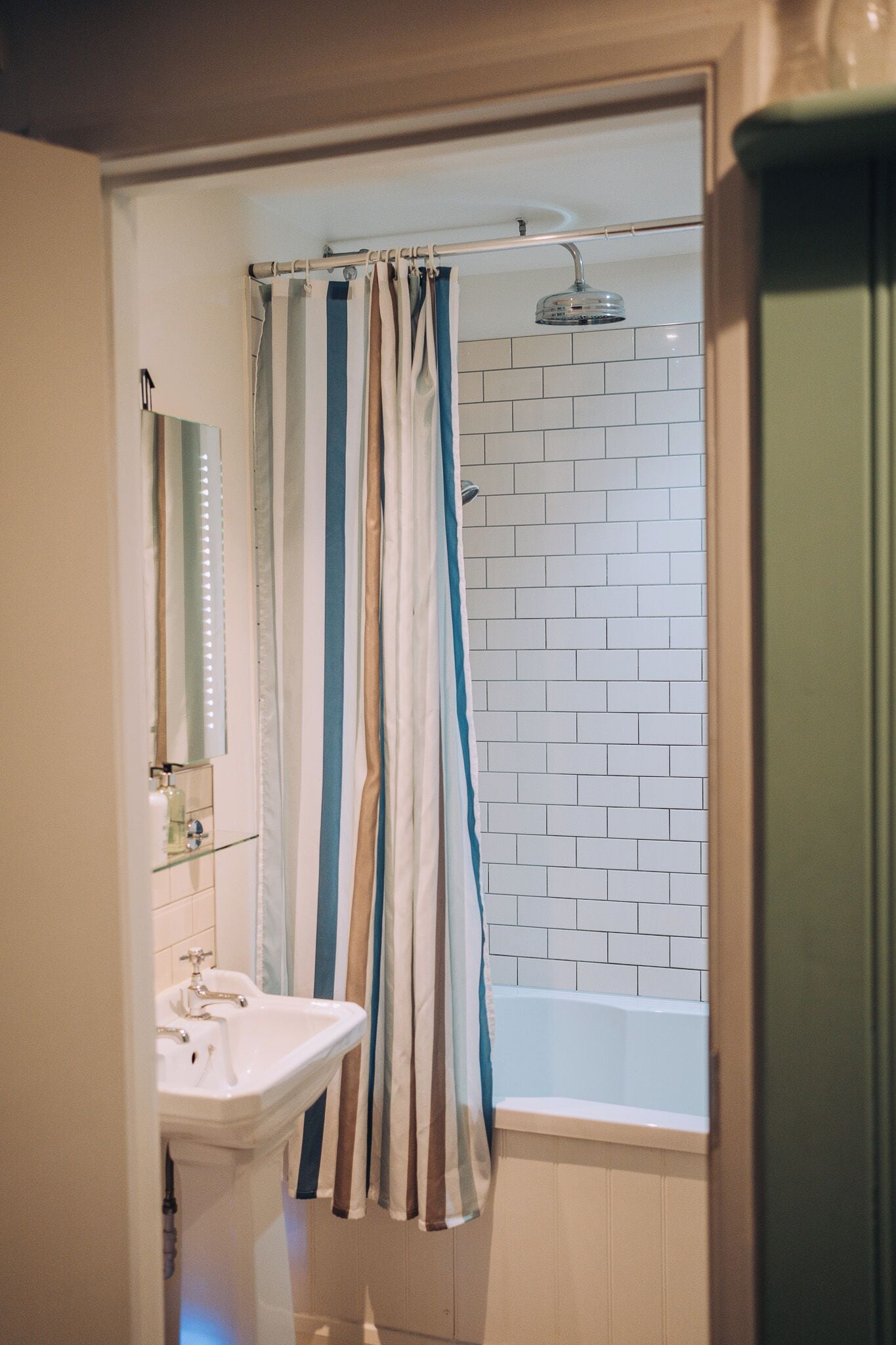 A bathroom with a white sink, a mirror, a shower curtain, and a white tiled wall.