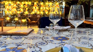 An outdoor dining table with a clear glass wine glass, a folded napkin, and cutlery. - AgriBarocco (Noto)