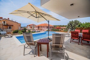 Relax by the clear pool surrounded by a deck and shaded seating area.