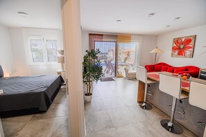 Relax in a serene space with a neatly made bed, a potted plant, and a red sofa.