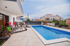 Relax by the pool in a serene outdoor space surrounded by lush greenery and a clean-lined design.