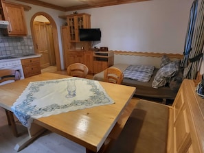 A cozy kitchen with wooden cabinets, a dining table with a lace tablecloth, and a sofa with plaid blankets.