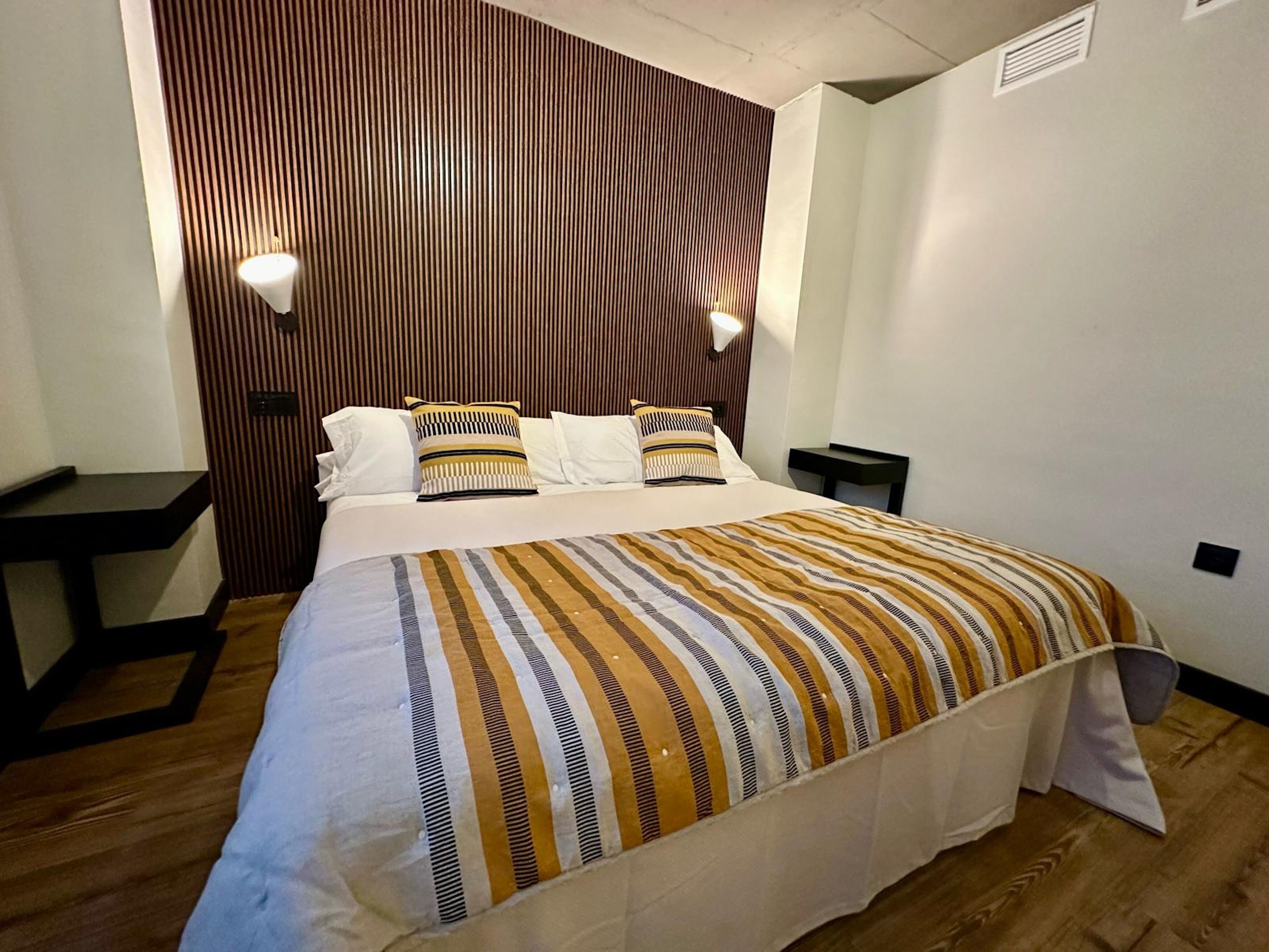 A neatly made bed with striped bedding, a wooden headboard, and bedside lamps.