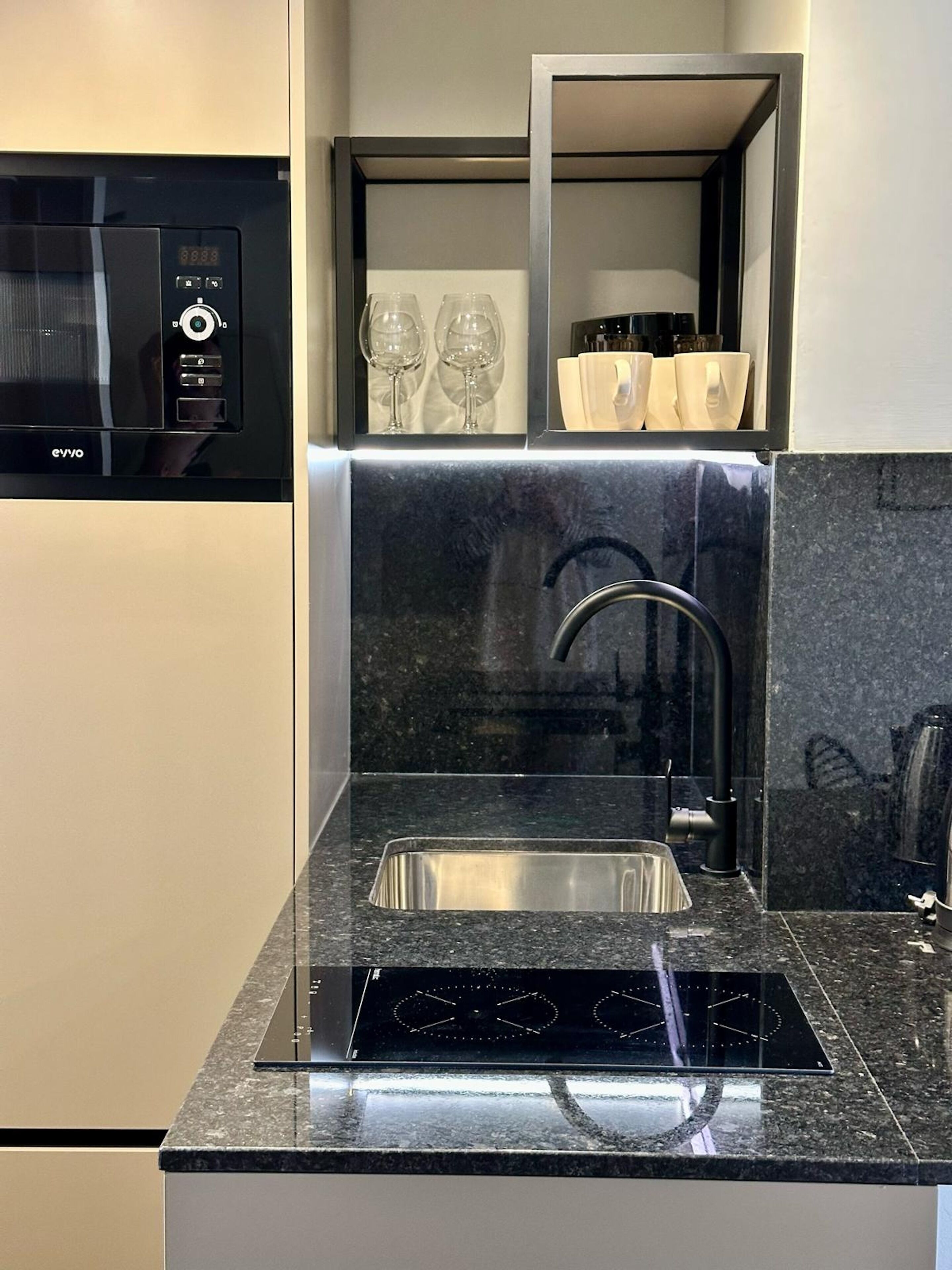 A modern kitchen with a built-in microwave, a stainless steel sink, and a black stovetop.