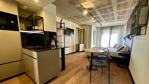 A modern kitchen with a central island, a dining area with a table and chairs, and a bedroom with a bed and a TV. - BUBU Apartments By Exclusive Homes (Málaga)