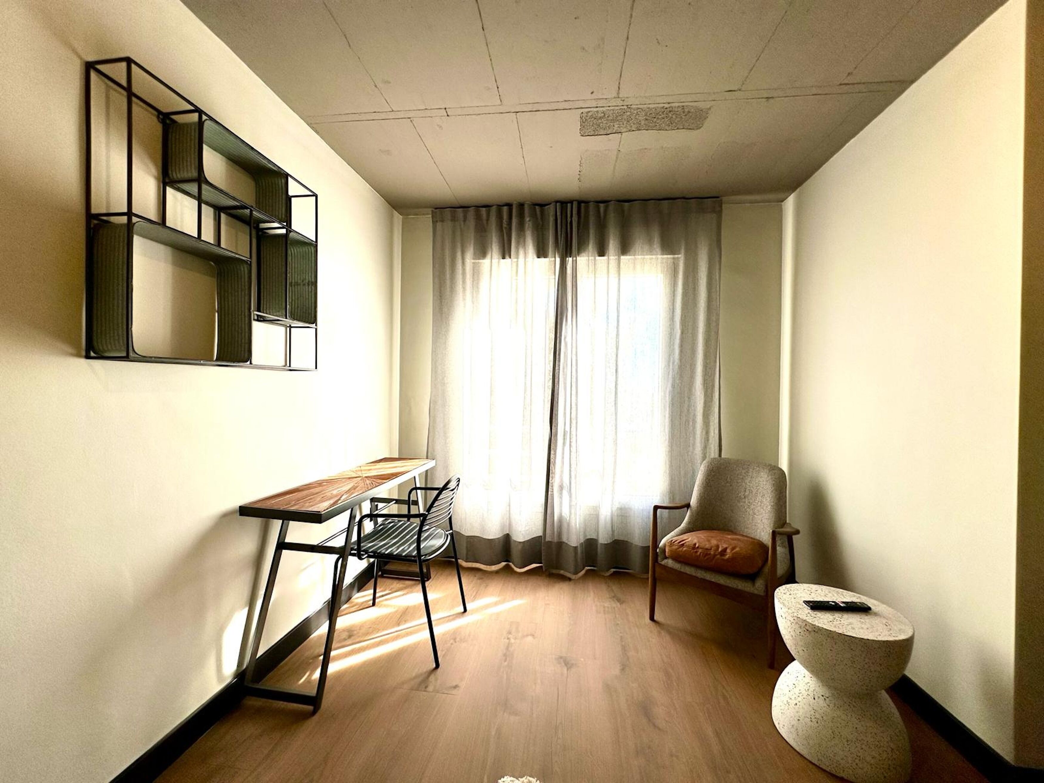 Una habitación pequeña con escritorio, silla y un taburete.