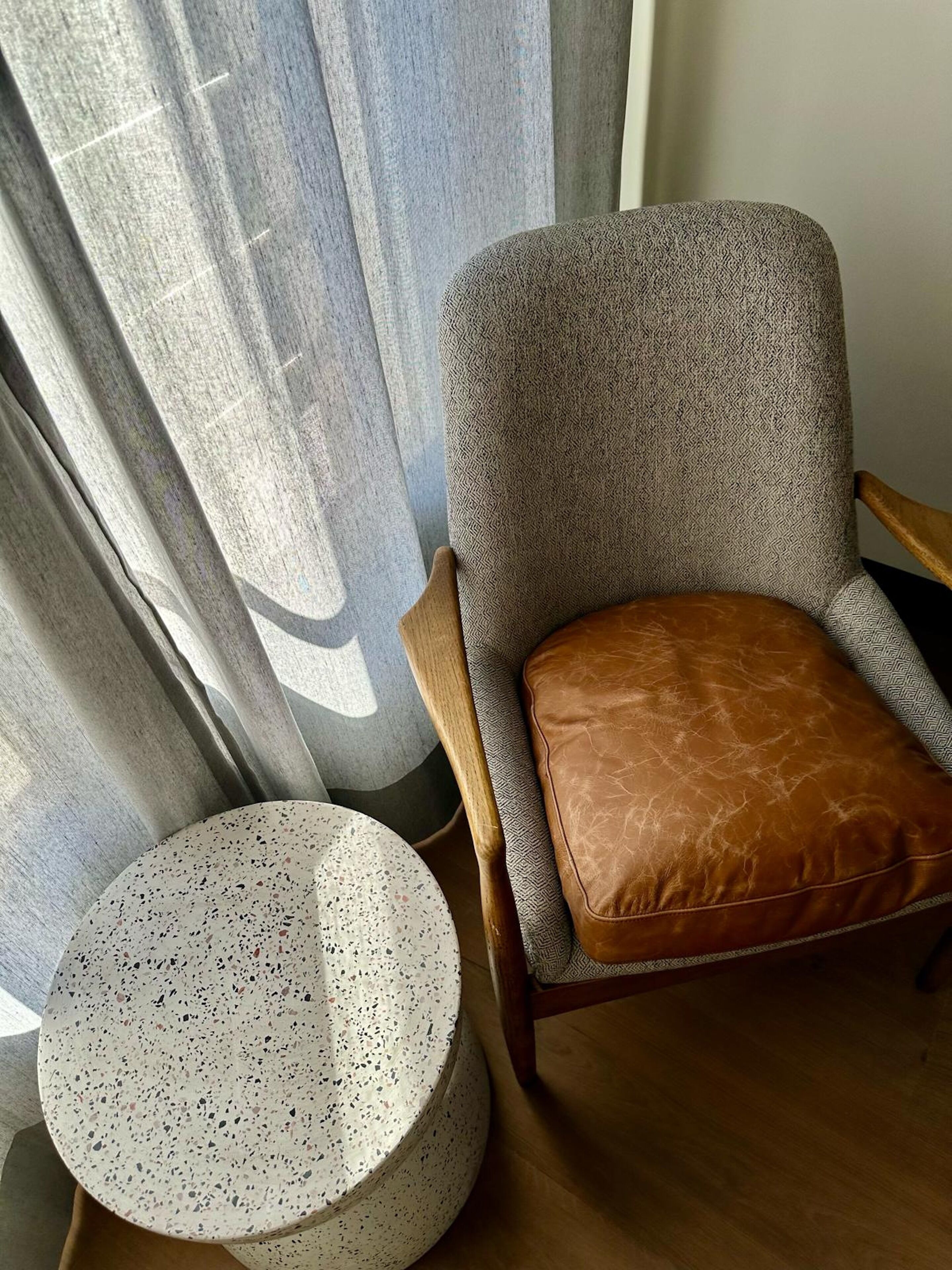 Tuoli, jossa on kuvioitu kangasverhoilu ja ruskea nahkainen istuintyyny, on sijoitettu pyöreän, täplikkään pöydän viereen.