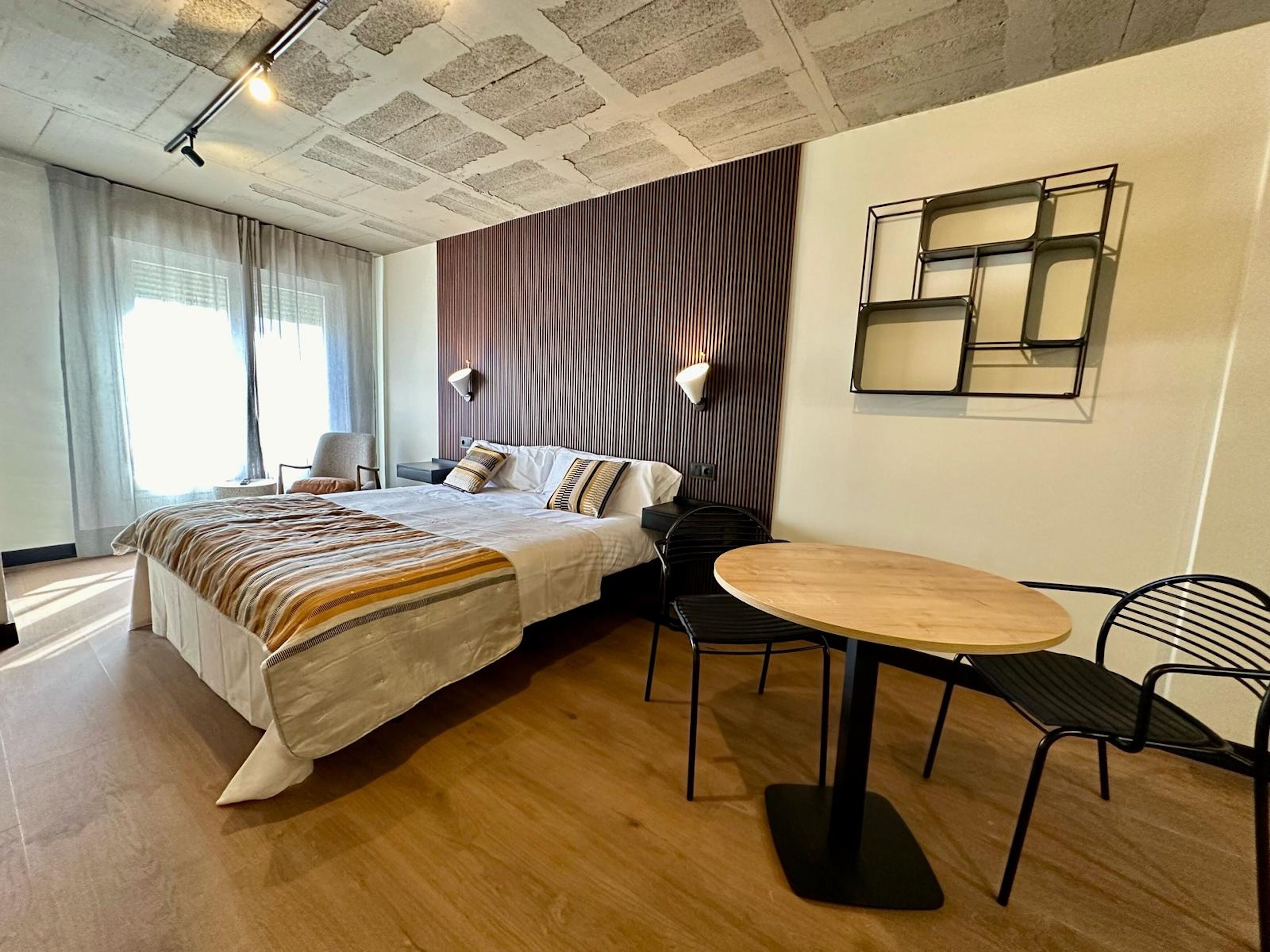 A modern hotel room with a large bed, a round wooden table, and two chairs.