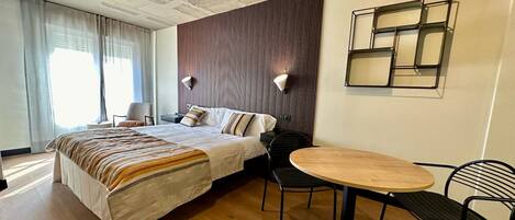 A modern hotel room with a large bed, a round wooden table, and two chairs.
