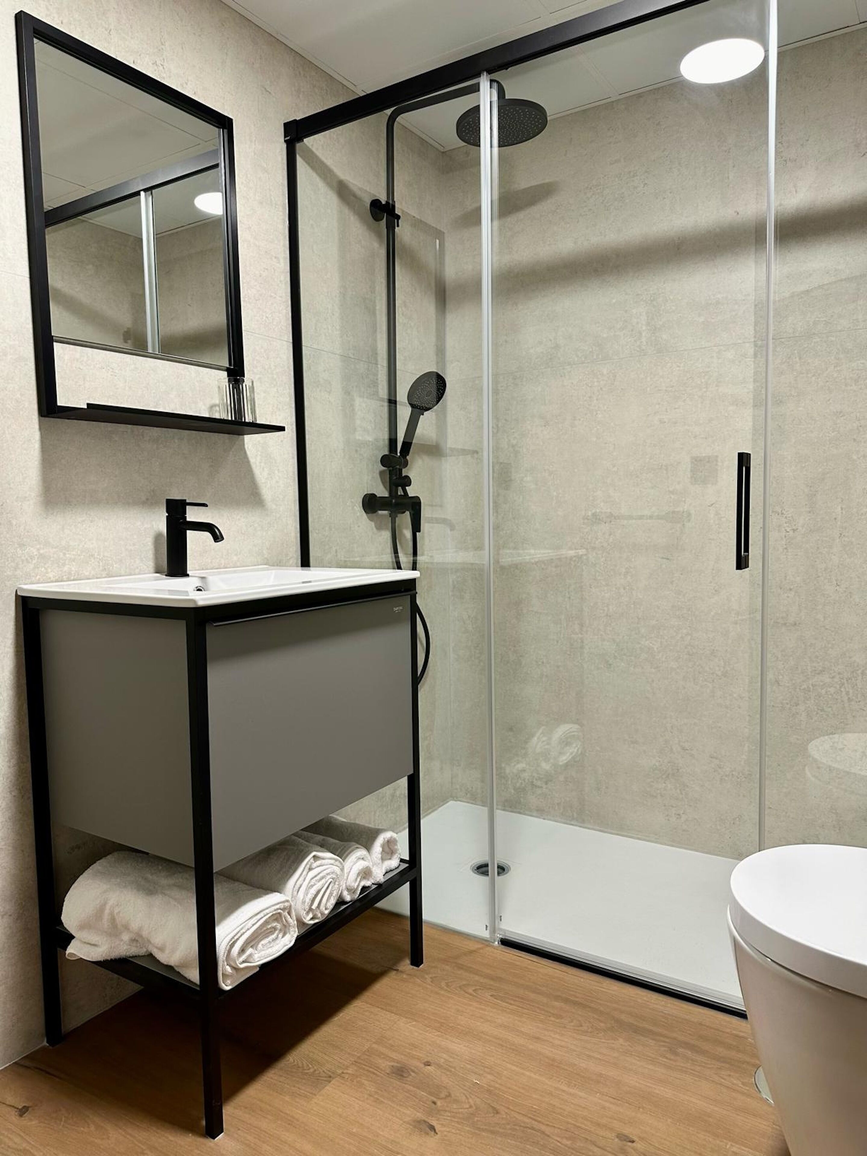A modern bathroom with a glass-enclosed shower, a white sink with a black frame, and a mirror above the sink.