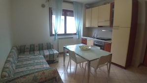 A small, compact kitchen with basic amenities, a dining table with chairs, and a sofa with a floral pattern. - CLEO CAMELIA (Falconara Marittima)