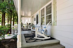 A porch with white railings, two Adirondack chairs, and a small table with a blue cushion.