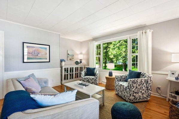 A living room with a sofa, armchairs, a coffee table, a cabinet, and a window with curtains.