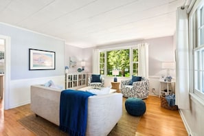 A room with a large bed, two chairs, a small table, and a window with a view of greenery.