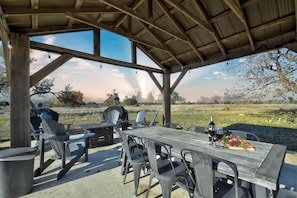 Eine überdachte Terrasse im Freien mit einem Holztisch, Stühlen und einem Grill.